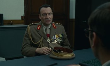 Movie still from “Z” (1969), directed by Costa-Gavras – A man in a military uniform sitting at a table; Medium shot, Low angle