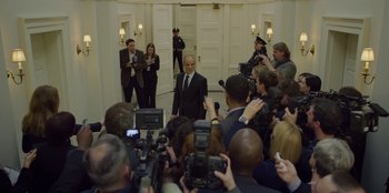 Movie still from “House of Cards” (2013), created by Beau Willimon – A man in a suit and tie surrounded by a crowd of people; Wide shot, High angle