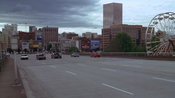Movie still from “Zero Effect” (1998), directed by Jake Kasdan – Cars driving down a city street under a cloudy sky; Extreme Wide shot, High angle