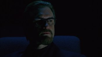 Movie still from “Zero Effect” (1998), directed by Jake Kasdan – A man with a goatee and glasses is sitting in a chair; Close Up shot, Low angle