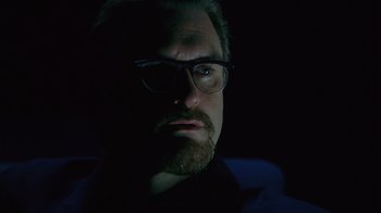 Movie still from “Zero Effect” (1998), directed by Jake Kasdan – A man with a goatee wearing glasses and a black shirt; Close Up shot, Over the shoulder angle