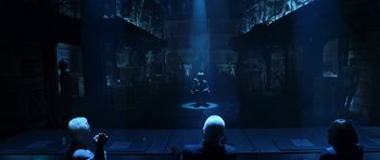 Movie still from “Zoolander” (2001), directed by Ben Stiller – A man sitting in front of a projection screen in a dark room; Wide shot, Over the shoulder angle