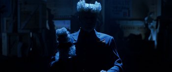 Movie still from “Zoolander” (2001), directed by Ben Stiller – A man holding a white dog in a dark room; Medium shot, Low angle