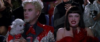 Movie still from “Zoolander” (2001), directed by Ben Stiller – A man and a woman wearing red and silver are sitting in front of a crowd of onlookers; Close Up shot, Low angle