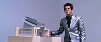 Movie still from “Zoolander” (2001), directed by Ben Stiller – A man standing next to a model of a building; Medium shot, Low angle