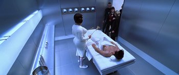 Movie still from “Zoolander” (2001), directed by Ben Stiller – A man laying on a bed in front of a group of people; Medium shot, High angle