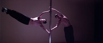 Movie still from “Zoolander” (2001), directed by Ben Stiller – A couple of men holding hands on a pole; Wide shot, Low angle