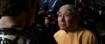 An older man in a yellow shirt is being interviewed by a camera