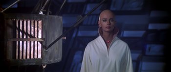 Movie still from “Star Trek: The Motion Picture” (1979), directed by Robert Wise – A bald woman in a white shirt is standing next to a lamp; Close Up shot, Over the shoulder angle