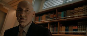 Movie still from “Superman Returns” (2006), directed by Bryan Singer – A bald man in a suit and tie in front of a book shelf; Close Up shot, Low angle