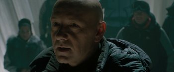 Movie still from “Superman Returns” (2006), directed by Bryan Singer – A bald man in a black jacket is looking at the camera; Close Up shot, Over the shoulder angle