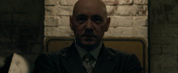 Movie still from “Superman Returns” (2006), directed by Bryan Singer – A man with a bald head wearing a suit and tie; Close Up shot, Low angle