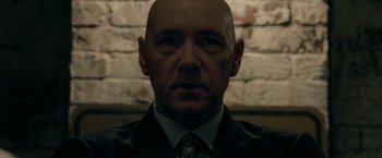 Movie still from “Superman Returns” (2006), directed by Bryan Singer – A man with a bald head wearing a suit and tie; Close Up shot, Low angle