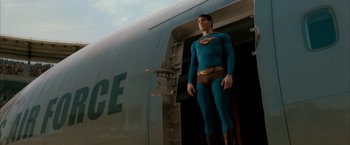 Movie still from “Superman Returns” (2006), directed by Bryan Singer – A man in a superman costume standing in front of an airplane; Wide shot, Low angle