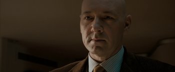 Movie still from “Superman Returns” (2006), directed by Bryan Singer – A bald man in a suit and tie looking at the camera; Close Up shot, Low angle