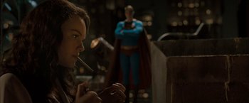 Movie still from “Superman Returns” (2006), directed by Bryan Singer – A woman smoking a cigarette in front of a statue of superman; Medium shot, Over the shoulder angle