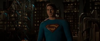 Movie still from “Superman Returns” (2006), directed by Bryan Singer – A man in a superman costume standing next to a building; Medium shot, Over the shoulder angle