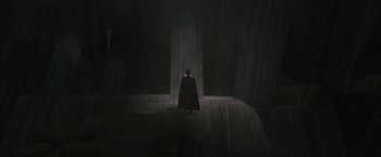 Movie still from “Superman Returns” (2006), directed by Bryan Singer – A man in a black cape stands in a dark room; Extreme Wide shot, Low angle