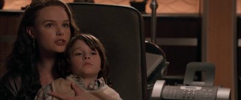 Movie still from “Superman Returns” (2006), directed by Bryan Singer – A young child sitting in a chair next to an adult; Close Up shot, Over the shoulder angle