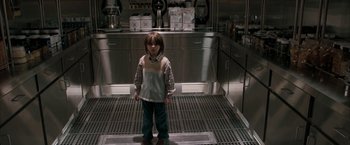 Movie still from “Superman Returns” (2006), directed by Bryan Singer – A young boy standing in a kitchen in front of a counter; Wide shot, High angle