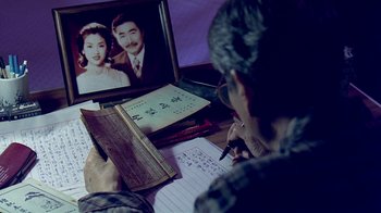 Movie still from “Eat Drink Man Woman” (1994), directed by Ang Lee – A man writing on a book while looking at an image of a man and a woman; Extreme Close Up shot, High angle