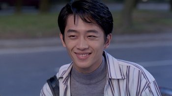Movie still from “Eat Drink Man Woman” (1994), directed by Ang Lee – A young man smiles for the camera while standing on the side of the road; Close Up shot, High angle