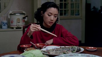 Movie still from “Eat Drink Man Woman” (1994), directed by Ang Lee – A woman sitting at a table with a plate of food and chopsticks in front of her; Medium shot, Over the shoulder angle