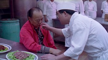 Movie still from “Eat Drink Man Woman” (1994), directed by Ang Lee – A man in a chef's outfit is feeding food to another man in an apron; Close Up shot, High angle