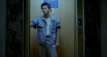 Movie still from “Rebels of the Neon God” (1992), directed by Tsai Ming-liang – A man in a denim jacket standing next to an elevator; Medium shot, Low angle