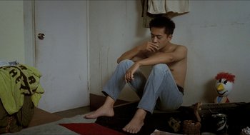 Movie still from “Rebels of the Neon God” (1992), directed by Tsai Ming-liang – A man sitting on the ground with his feet crossed; Medium shot, Low angle