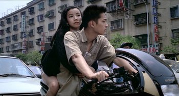 Movie still from “Rebels of the Neon God” (1992), directed by Tsai Ming-liang – A man and a woman riding a bike together; Medium shot, High angle