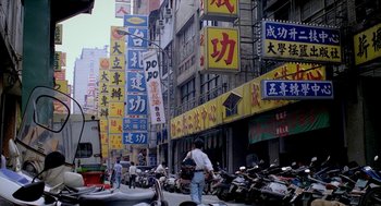 Movie still from “Rebels of the Neon God” (1992), directed by Tsai Ming-liang – A man standing next to a motorcycle on a street; Extreme Wide shot, High angle