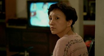 Movie still from “Rebels of the Neon God” (1992), directed by Tsai Ming-liang – A woman in a pink sweater is looking at a television; Close Up shot, Over the shoulder angle