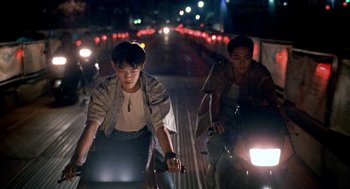Movie still from “Rebels of the Neon God” (1992), directed by Tsai Ming-liang – Two young men riding bikes down a street at night; Wide shot, High angle