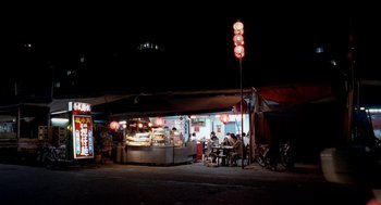 Movie still from “Rebels of the Neon God” (1992), directed by Tsai Ming-liang – People are sitting at tables outside of a restaurant at night; Extreme Wide shot, High angle