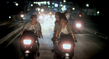Movie still from “Rebels of the Neon God” (1992), directed by Tsai Ming-liang – A group of young people riding motorcycles down a street at night; Wide shot, High angle