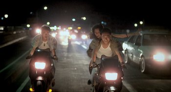 Movie still from “Rebels of the Neon God” (1992), directed by Tsai Ming-liang – A group of young people riding motorcycles down a street at night; Wide shot, High angle