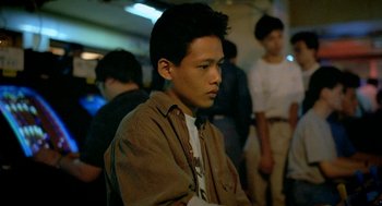Movie still from “Rebels of the Neon God” (1992), directed by Tsai Ming-liang – A young man is sitting in a room with other people; Medium shot, High angle