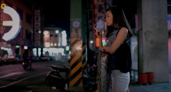 Movie still from “Rebels of the Neon God” (1992), directed by Tsai Ming-liang – A woman standing on the side of the road looking at her cell phone; Medium shot, Low angle