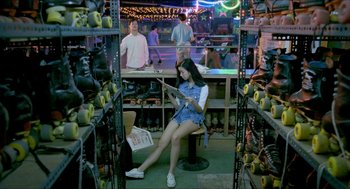 Movie still from “Rebels of the Neon God” (1992), directed by Tsai Ming-liang – A woman sitting on a chair in a room filled with fruit; Wide shot, High angle