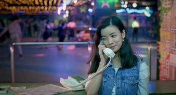 Movie still from “Rebels of the Neon God” (1992), directed by Tsai Ming-liang – A woman holding a phone to her ear while sitting at a table in front of lights; Close Up shot, High angle