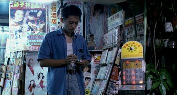 Movie still from “Rebels of the Neon God” (1992), directed by Tsai Ming-liang – A man standing in front of a store looking at his phone; Medium shot, High angle