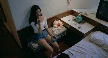 Movie still from “Rebels of the Neon God” (1992), directed by Tsai Ming-liang – A woman sitting on a bed holding a cell phone; Medium shot, High angle