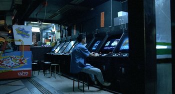 Movie still from “Rebels of the Neon God” (1992), directed by Tsai Ming-liang – A man sitting in front of a row of arcade machines; Wide shot, High angle