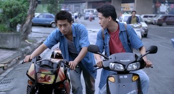 Movie still from “Rebels of the Neon God” (1992), directed by Tsai Ming-liang – Two young men riding motorcycles down a street; Medium shot, High angle