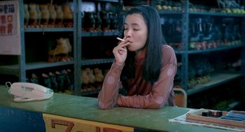 Movie still from “Rebels of the Neon God” (1992), directed by Tsai Ming-liang – A woman sitting at a counter smoking a cigarette; Medium shot, High angle