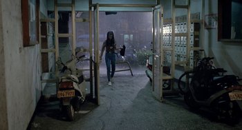 Movie still from “Rebels of the Neon God” (1992), directed by Tsai Ming-liang – A woman is walking through a doorway in a garage; Wide shot, High angle