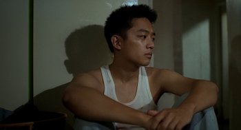 Movie still from “Rebels of the Neon God” (1992), directed by Tsai Ming-liang – A man sitting in a room with his hands on his chest; Close Up shot, Low angle