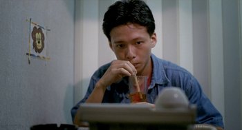 Movie still from “Rebels of the Neon God” (1992), directed by Tsai Ming-liang – A man sitting in front of a computer drinking a beverage; Close Up shot, High angle