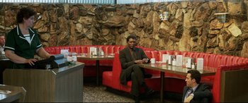 Movie still from “xXx” (2002), directed by Rob Cohen – A man sitting on a red bench in a restaurant; Wide shot, High angle